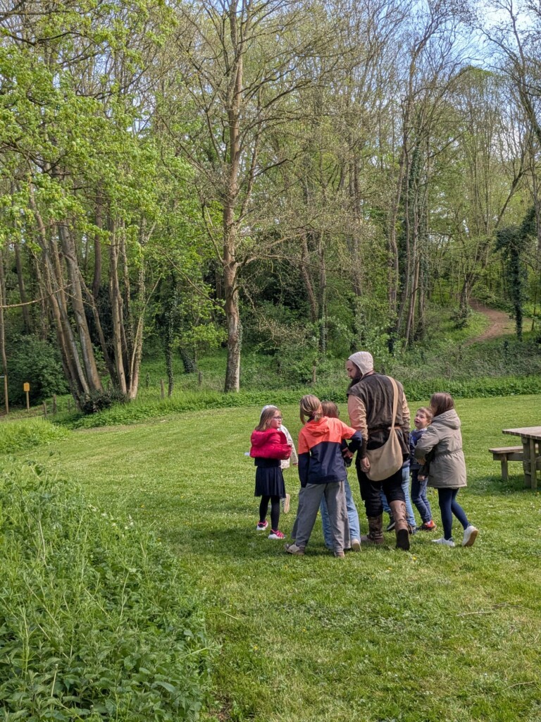 Des enfants écoutent un animateur dans un parc verdoyant de Feuguerolles-Bully.