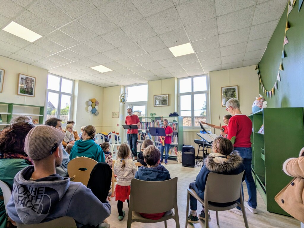 Animation musicale dans une bibliothèque, avec des enfants et des adultes écoutant des performances instrumentales.