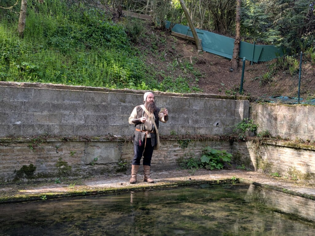 Homme au bord d'un bassin, entouré de verdure, exécutant une activité artisanale dans un cadre rural.