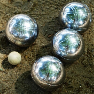 Boules de pétanque sur le sable, avec une petite boule blanche au centre.