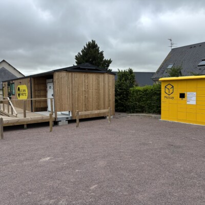 Cabane en bois et consigne jaune pour retraits de colis, situées dans un espace communal à Feuguerolles-Bully.